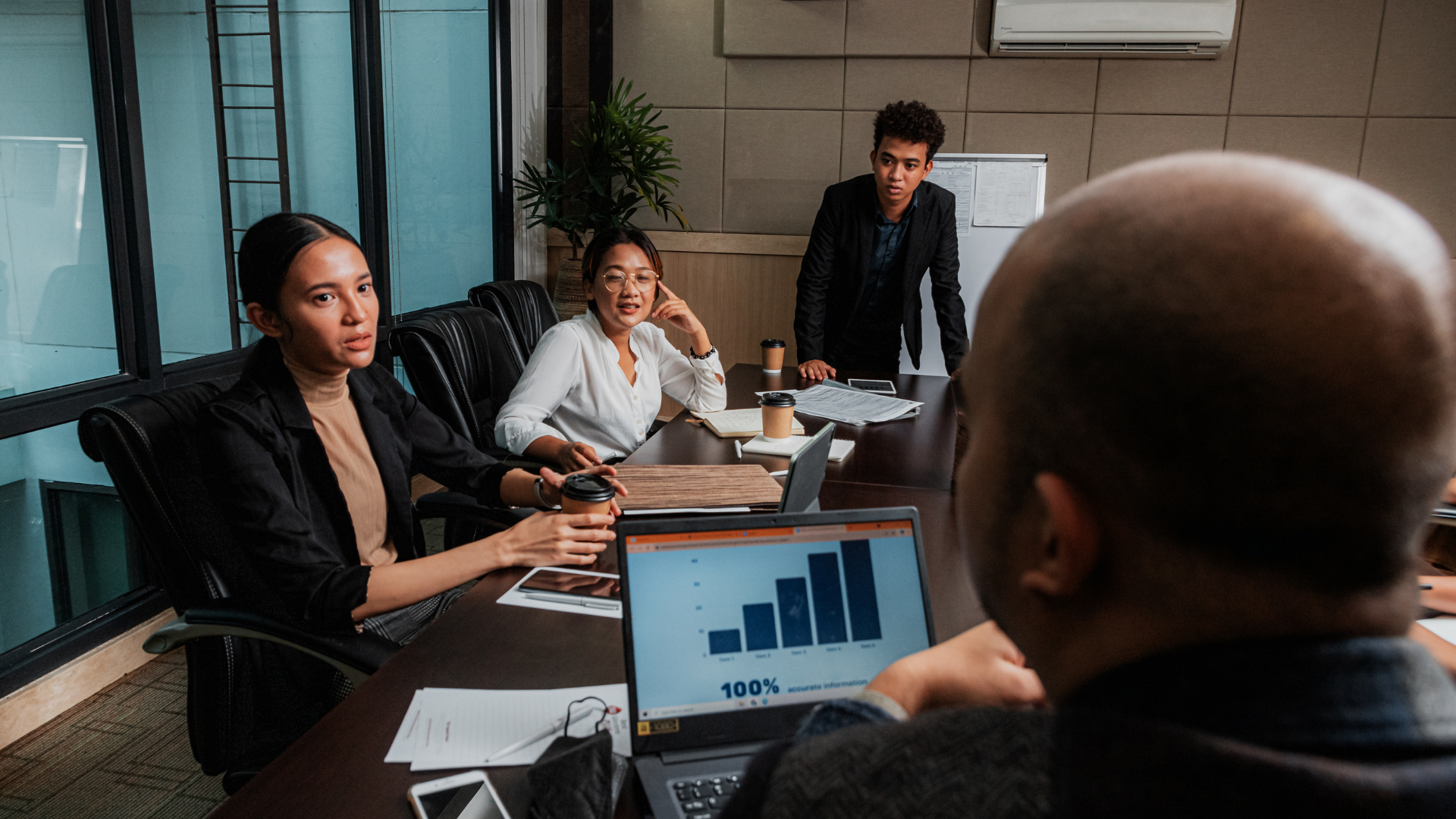 Co-workers around a conference table with a laptop showing charts