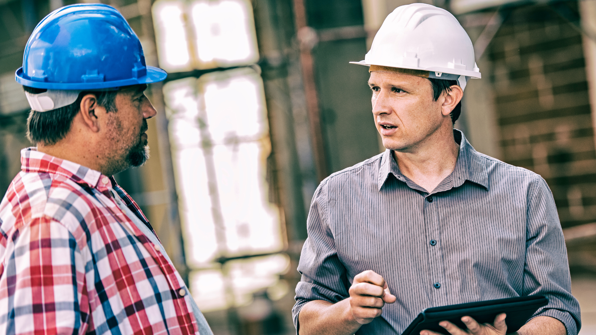 Two construction workers on site wearing hard hats, holding a tablet