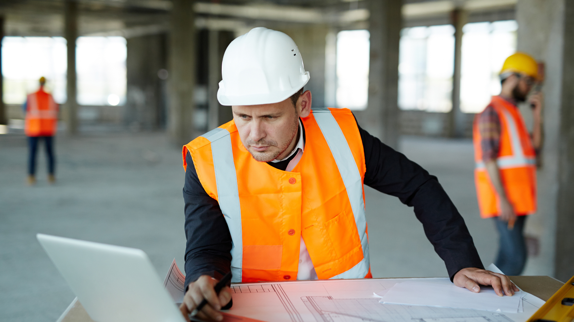 A construction worker on site, looking at CRM on laptop