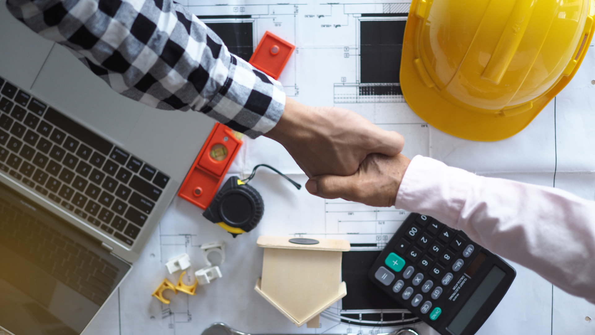 Two people shaking hands over a construction deal