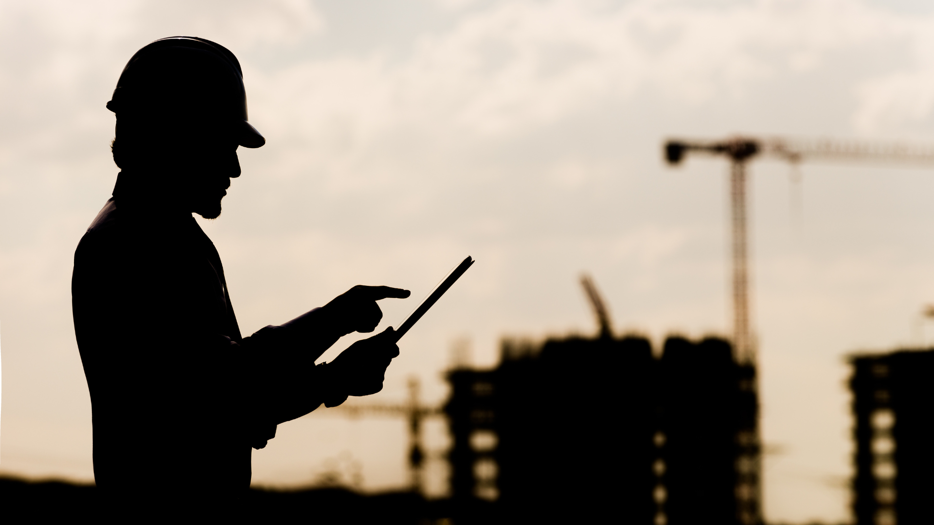 A construction worker's silhouette on site, working from a tablet 