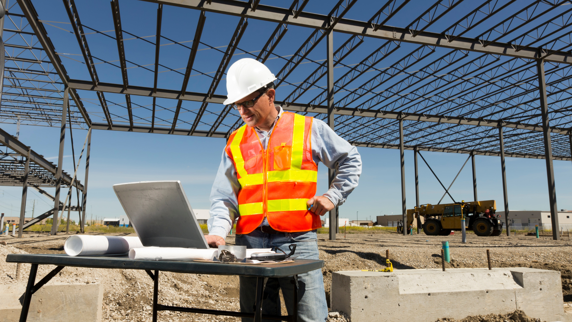 A construction worker on site, using a laptop on a table 