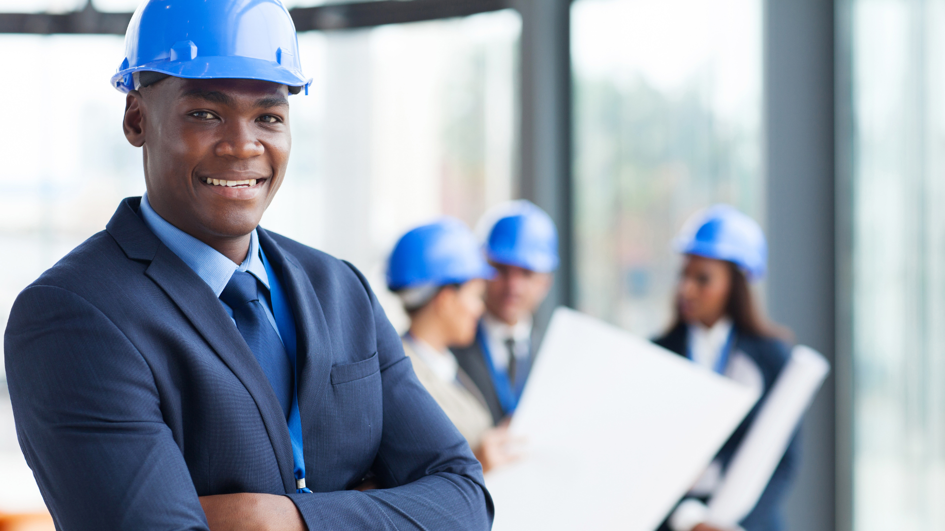 A construction person in a hard hat with colleagues blurred in the background
