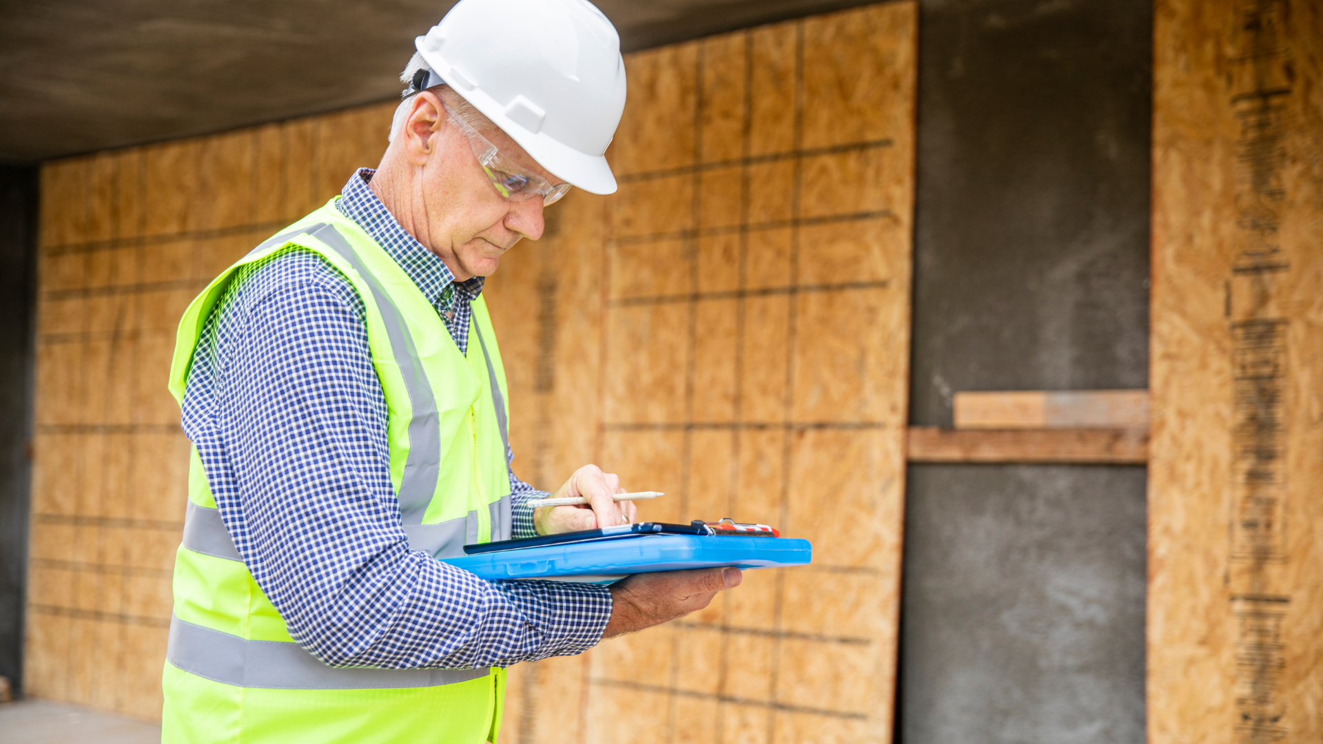 An older, male construction worker wearing a hard hat using a tablet on site